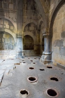 Stone room with large floor holes and massive pillars surrounded by weathered walls, Haghpat