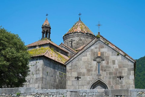 Massive stone church towers with cross-decorated roofs surrounded by a clear sky, Haghpat