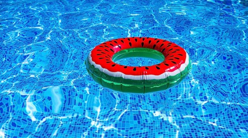 A bright ring-a float, with a watermelon, in the clear blue water of the pool, under the sunlight