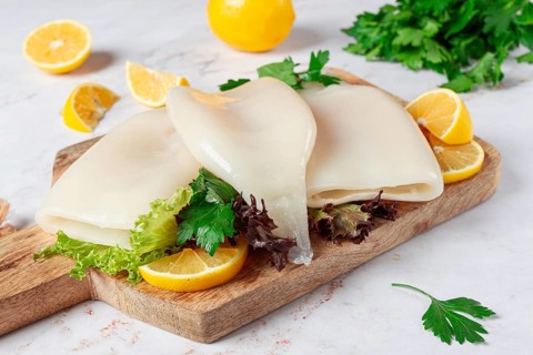 Fresh squid prepared for cooking, surrounded by herbs and lemon, placed on a wooden chopping board
