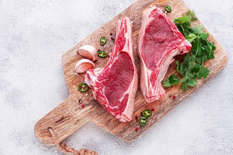Fresh pieces of beef on the bone, on a wooden cutting board, with herbs and spices, ready for