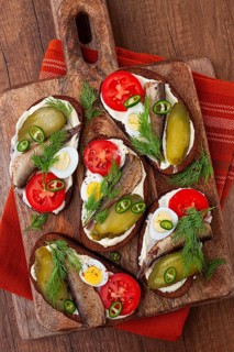Sandwiches on rye bread with sprats, quail eggs, fresh tomatoes and pickled cucumber, on a wooden
