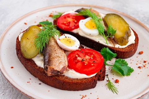 Sandwiches on rye bread, with sprats, quail eggs, fresh tomatoes and pickled cucumber, appetizer,