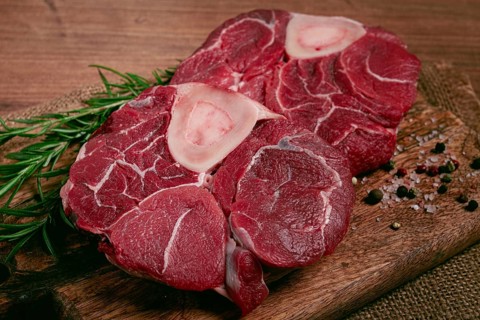 Knuckle on the bone, raw meat for ossobuco, on a wooden chopping board, with a sprig of rosemary,