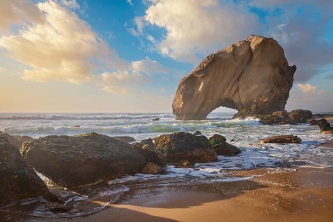 Penedo do Guincho, a large boulder rock arch at Praia da Santa Cruz, Portugal, with ocean waves and