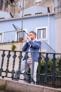 Man musician in a blue blazer and white sweater playing blues on a harmonica with eyes closed,