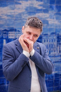 Man musician in a blue blazer and white sweater playing blues on a harmonica with eyes closed,