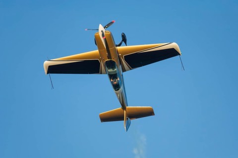 Golden stunt aerobatic plane performing stunts in blue sky. Concept of speed, difficulty,