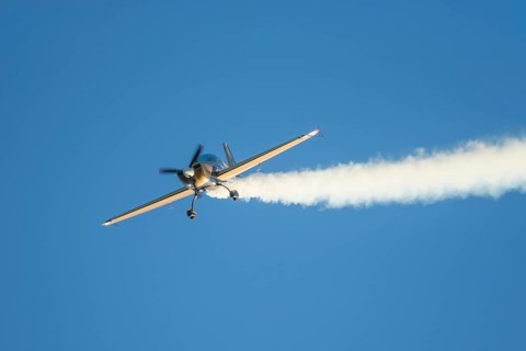 Golden stunt aerobatic plane performing stunts in blue sky with smoke trail. Concept of speed,