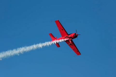 Red stunt aerobatic plane performing stunts in blue sky. Concept of speed, difficulty, precision,