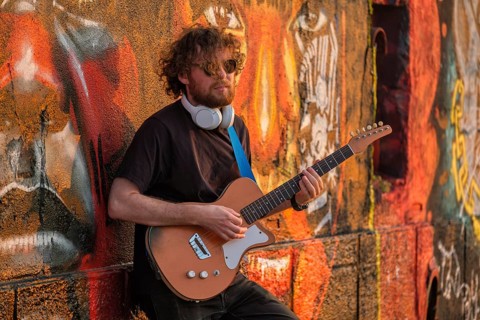 Hipster street musician in black playing electric guitar in the street on sunset leaning on a