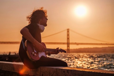 Hipster street musician in black playing electric guitar in the street on sunset