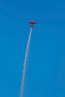Red stunt aerobatic plane performing stunts in blue sky. Concept of speed, difficulty, precision,