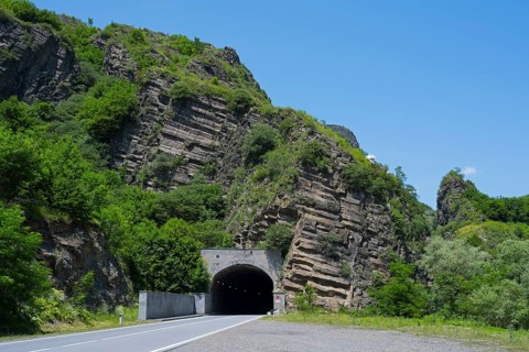 A tunnel in a rocky, green landscape under a clear blue sky, road tunnel, Debed gorge, Lorikeet
