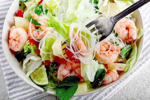 Thai salad with shrimp and rice noodles, pineapple slices, coriander and mint leaves, on a white