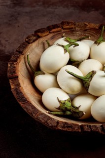 White mini eggplant, in a wooden bowl, on the table, close-up