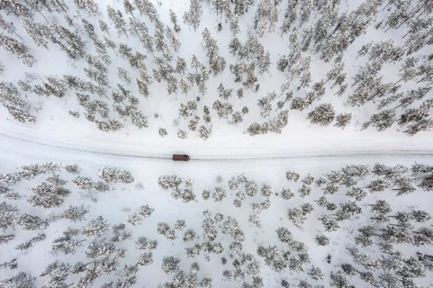 Aerial view over car, van driving over snow covered road through the taiga in winter, Riisitunturi