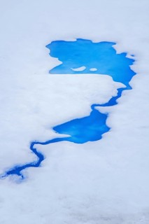 Aerial view over vivid blue water of meltpond / melt pond / meltwater pool on sea ice in the Arctic