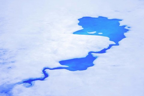 Aerial view over vivid blue water of meltpond / melt pond / meltwater pool on sea ice in the Arctic