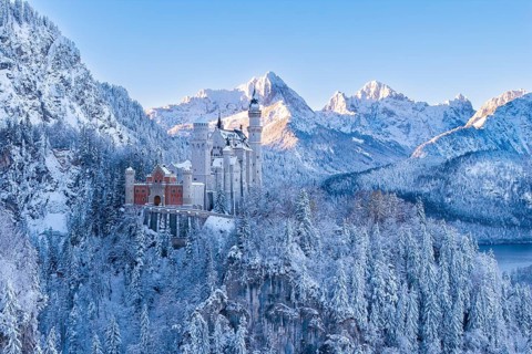 Wintery Neuschwanstein Castle in a snowy mountain landscape. Bright sun rays on the peaks,