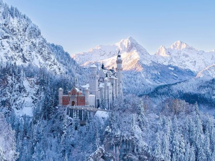 Neuschwanstein Castle in winter, surrounded by snow-covered trees and picturesque mountains.