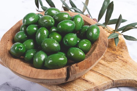 Halkidiki olives, classic Greek green olives, in a wooden bowl, on a cutting board, top view,