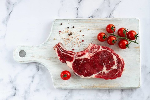 Raw rib eye steak, cowboy steak, on a white wooden chopping board, marble table, top view, no