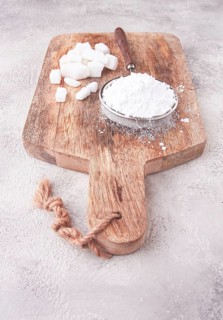 A strainer with powdered sugar, on a wooden cutting board, with pieces of white sugar