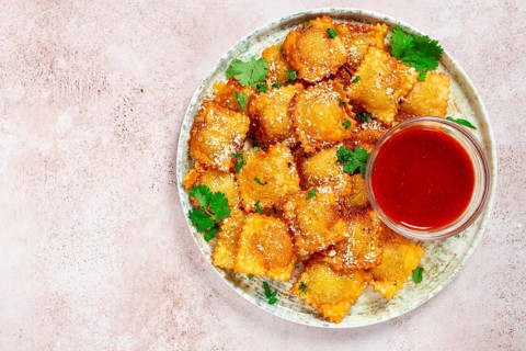 Fried ravioli with parmesan cheese, served with red sauce and garnished with herbs, on a light