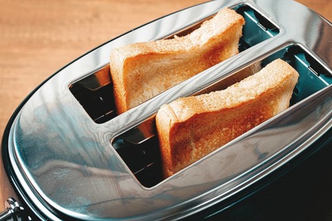 Two slices of bread are toasting in a shiny metal toaster, set on a countertop in a warm kitchen.