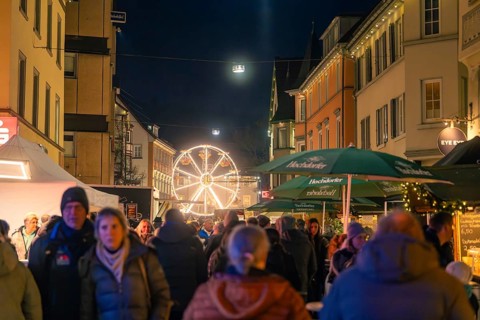 A Ferris wheel in the distance illuminates a busy street of a Christmas market, Christmas market