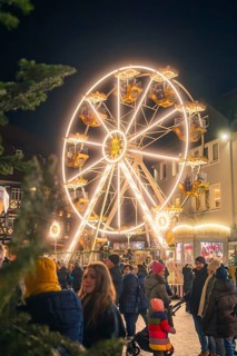 A brightly lit Ferris wheel rises above a crowd at a Christmas market, Christmas market 2025,