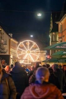 An illuminated Ferris wheel on a night-time Christmas market full of people, Christmas market 2025,