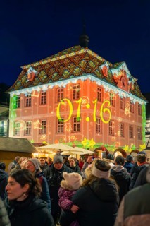 Colourfully illuminated building with time projection on a busy Christmas market at night,