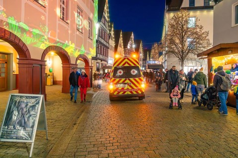 Busy Christmas market at night with rescue service vehicle and festive lighting, Christmas market