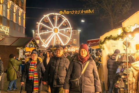 People stroll through an illuminated market with a large Ferris wheel in the background, Christmas