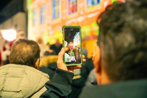 People watch a colorful event, with some capturing the scene with smartphones, Christmas market