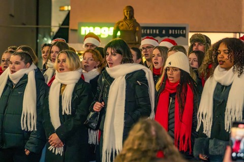 A choir sings outside, the singers wear warm clothes and atmospheric hats and scarves, Christmas