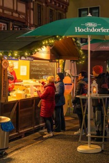 People stand at a well-lit stand to buy pastries at a Christmas market, Christmas market 2025,