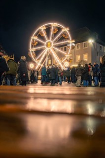 People enjoy the illuminated Ferris wheel on a cobblestone square at night, Christmas market 2025,
