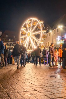 People walk across a square with illuminated Ferris wheel at night, Christmas market 2025, Nagold,