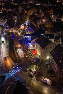 Aerial view of an illuminated Christmas market at night with a shiny Christmas tree and crowds of