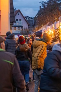 Visitors to a busy market stroll through festive lighting, Aidlingen Christmas Market, Böblingen