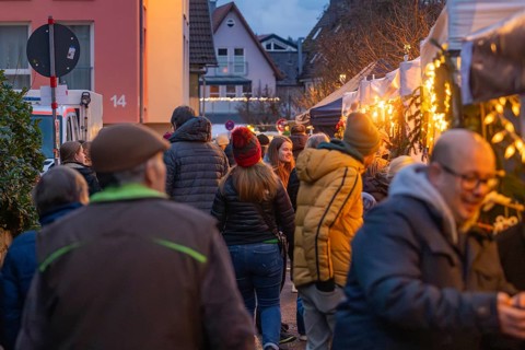 People stroll through an illuminated night market in a street, Aidlingen Christmas market,