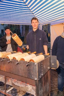 A market stand selling tree strips. A smiling person shows a tree striezel, Aidlingen Christmas