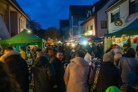 Closely packed visitors enjoy the evening market atmosphere between tents and lights, Aidlingen