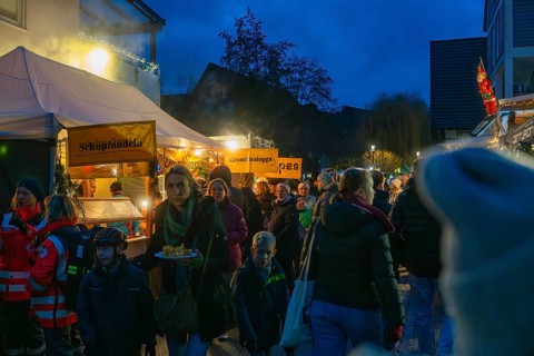 Families and children stroll through festively lit food stalls at a Christmas market in the