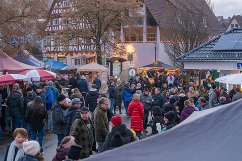 Lively Christmas market in front of half-timbered houses and trees, numerous visitors enjoy the