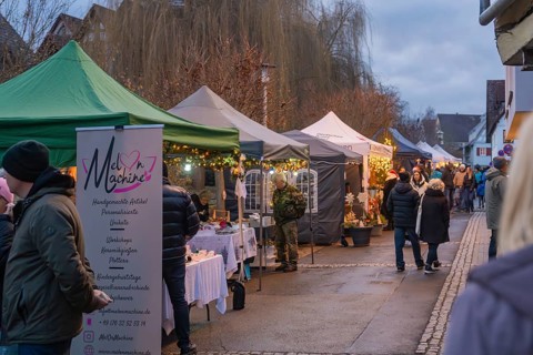 People stroll through a market with various illuminated stands in the evening, Aidlingen Christmas