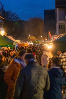 People stroll between glowing market stalls and trees at the Christmassy evening market, Aidlingen